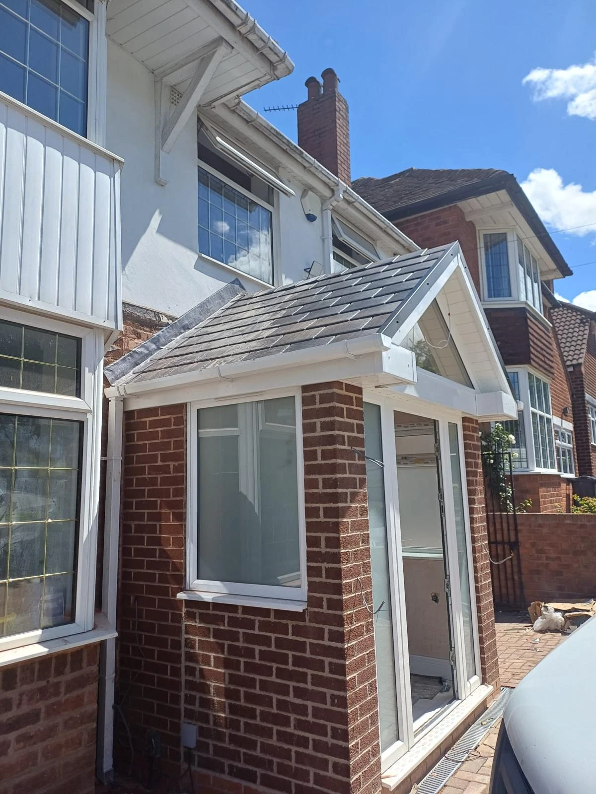 Brick porch with white-framed windows and a tiled gabled roof attached to a house on a sunny day.
