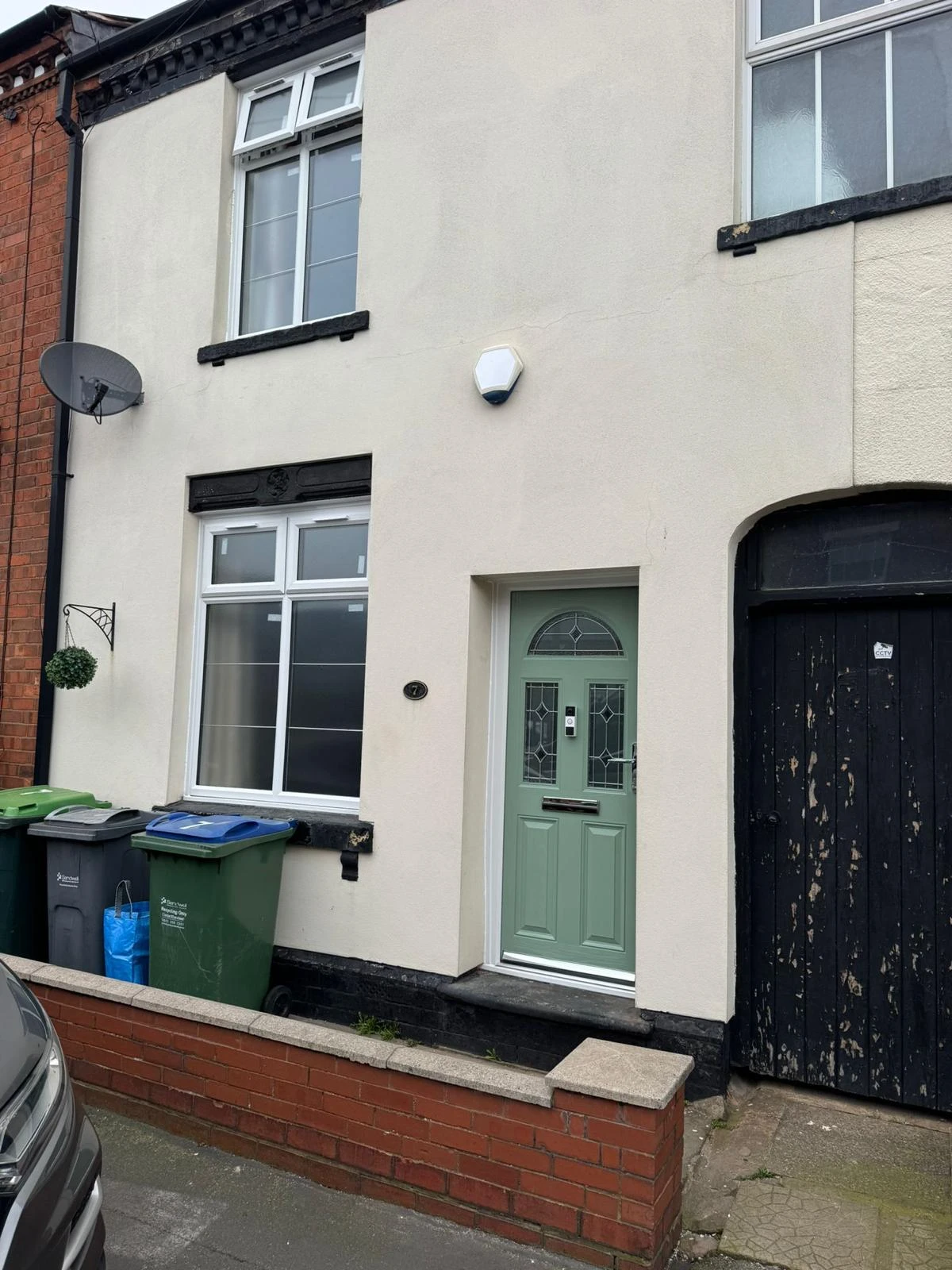 Exterior of a two-story house featuring a mint green front door, satellite dish, and trash bins, with a black door to the side.