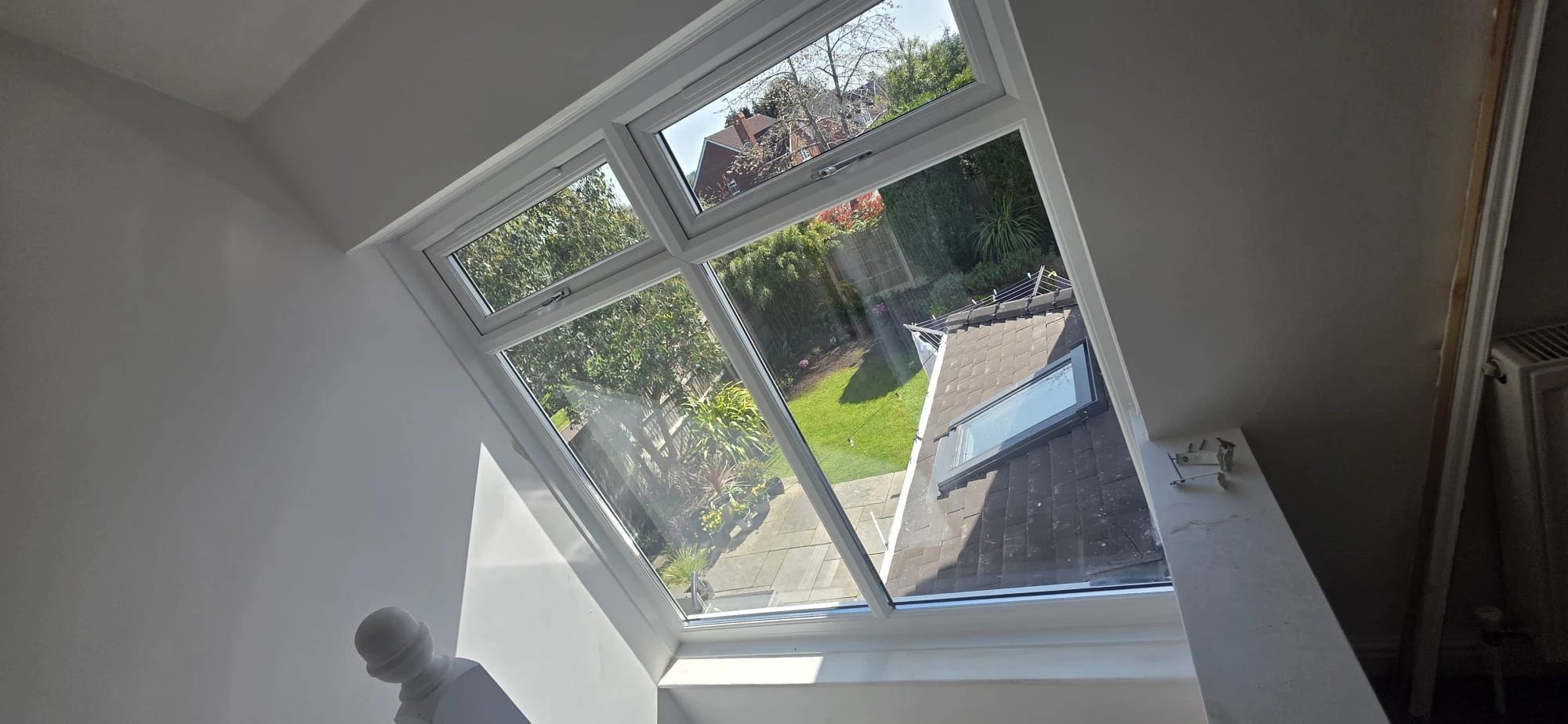 Bright interior view through a large window, showcasing a garden and patio with greenery and colorful plants.